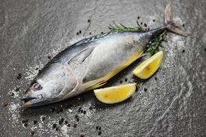Fresh fish with herbs spices rosemary and lemon - Raw fish seafood on black plate background top view , Longtail tuna , Eastern little tuna fish photo