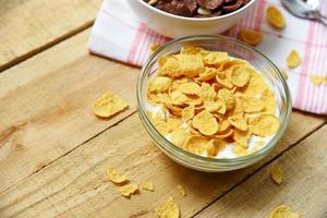 Copos de maíz en un tazón con leche sobre fondo de madera para el desayuno saludable de cereales foto