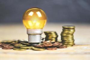 light bulb with light from the lamp on stacked coins on a wooden table background - energy saving idea , power saving and the world concept photo