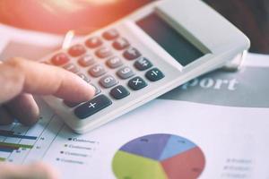 Business man using calculator for report financial statistics documents on infographics at office table close up - Sales report concept photo