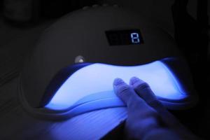 Closeup view of female hands with gel polish manicure. Woman puts hand into led uv lamp for curing top cover of nailpolish. UV lamp, LED Nail photo