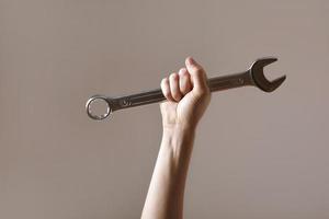 llave grande en la mano de la mujer. mano sostiene una llave sobre un fondo gris. llave combinada. llave grande de cromo vanadio en la mano. trabajo de mujeres. Día laboral.