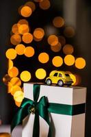 Little retro yellow toy model car with present gift box on gold bokeh background. Christmas, birthday, valentines day, delivery concept