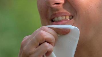 una chica de cabello rubio y corte de pelo corto se limpia los labios después de comer con una servilleta de papel cuadrada. de cerca foto