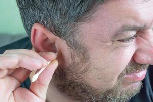 a man cleans his ears with a cotton swab photo