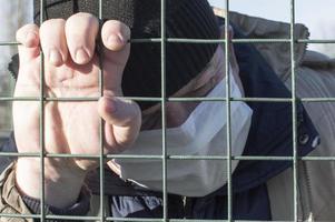 Pandemic. A man in a medical mask holds his hands on the bars. photo