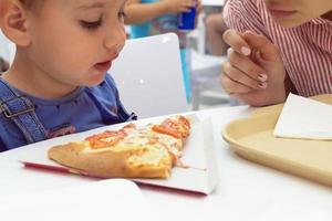 children teens eat pizza in a cafe where a lot of people photo