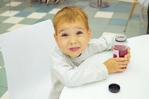 niño bebe jugo sentado en una mesa en el patio de comidas del centro comercial. foto