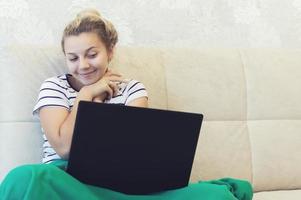 blonde girl is sitting at home on the couch with a laptop and communicates on the Internet. social networks. dating. photo