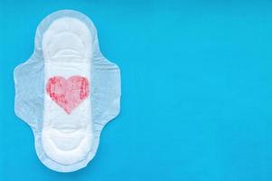 Women's pad with a red heart on a blue background. The concept of the menstrual cycle. photo