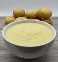 Mashed potatoes in a bowl, raw potatoes on background. photo