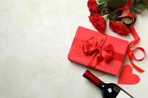 Concept of Valentine's day with roses, wine and gift box on white textured background photo