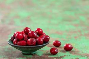 Fresh cranberries fruits in rustic asian bowl on old green wooden Background and daylight