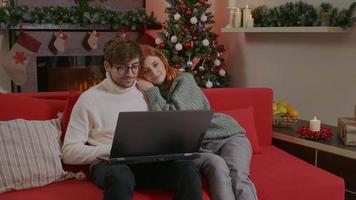 pareja en una casa decorada usando laptop en vacaciones hacer compras en línea. video