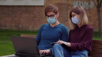 Two professional coworkers in protective mask discuss concentrating typing on laptop video