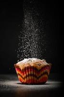 The cook sprinkles muffin with powdered sugar on a black background. photo