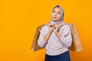 Portrait of beautiful asian woman holding shopping bags and looking sideways on yellow background photo