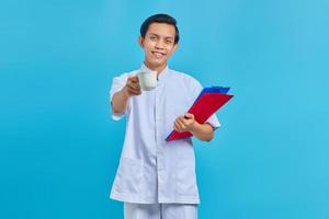 Smiling young male nurse holding folder and cup over blue background photo