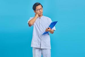 Portrait of male nurse holding clipboard and looking tired from work all day on blue background photo