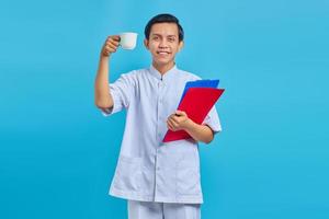 Smiling young male nurse holding folder and cup over blue background photo