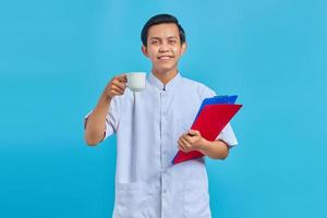 Smiling young male nurse holding folder and cup over blue background photo