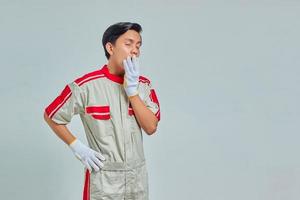 Portrait of handsome man wearing mechanical uniform feeling sleepy and covering mouth with hands isolated on gray background photo