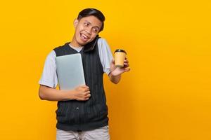 Smiling young handsome man talking on smartphone. carrying a laptop and holding a cup of coffee photo