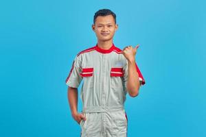 Portrait of happy young mechanic pointing finger at copy space on blue background photo