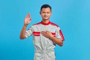 Portrait of handsome man wearing mechanical uniform swearing with hands on chest and open palms on blue background photo