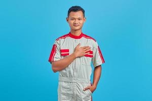 Portrait of smiling young Asian mechanic with palms on chest over blue background photo