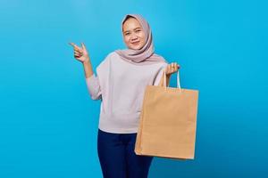 Portrait of cheerful asian woman holding shopping bag and pointing finger at empty space photo