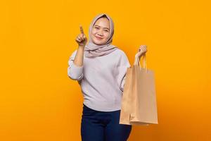 Portrait of smiling asian woman holding shopping bag and pointing finger at empty space photo