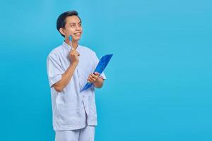 Handsome young male nurse concentrating thinking of ideas and smiling looking at empty space over blue background photo