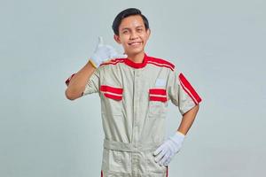 Portrait of cheerful handsome man wearing mechanical uniform showing approval with thumbs up gesture on gray background photo