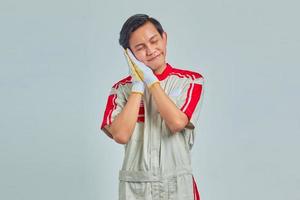 Portrait of cheerful handsome man wearing mechanical uniform with sleeping gesture on gray background photo