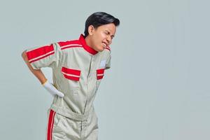 Handsome man wearing mechanic uniform suffering of backache and touching back with hand photo