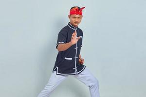 Foto de joven deportista vestido con kimono practicando karate aislado sobre fondo gris. mirando a la camara