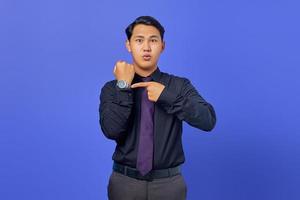 Handsome young businessman checking time on wristwatch on purple background photo