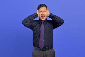 Frustrado joven empresario guapo cubriendo la oreja con expresión de ira sobre fondo púrpura foto