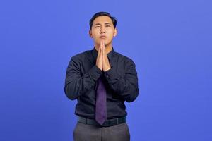 Retrato de tristeza joven asiático mostrando gesto de oración sobre fondo púrpura foto