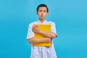 Happy young male nurse holding folder tightly and looking forward on blue background photo