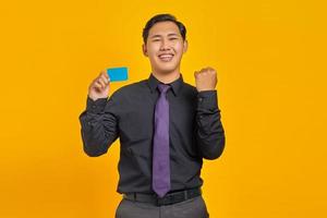 Portrait of excited cheerful young Asian businessman celebrating luck with credit card on hand photo