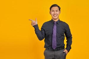 Smiling young Asian man pointing fingers at copy space on yellow background photo
