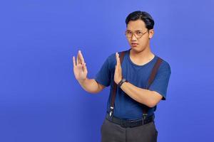 Portrait of nervous anxious young Asian man make stop don't move gesture over purple uebackground photo