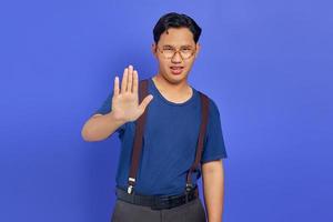 Retrato de hombre guapo enojado haciendo gesto de parada con las palmas de las manos sobre fondo púrpura foto