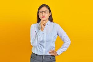 Pensive young beautiful business woman rubs chin and thinking question over yellow background photo