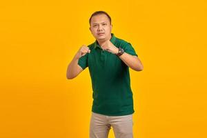 Portrait of angry young Asian man showing boxer gesture on yellow background photo