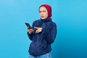 Angry young Asian woman using smartphone and looking at camera on blue background photo