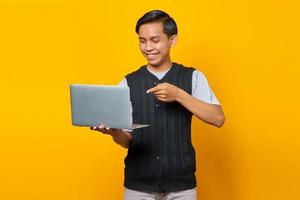 Cheerful handsome young man pointing laptop on yellow background photo