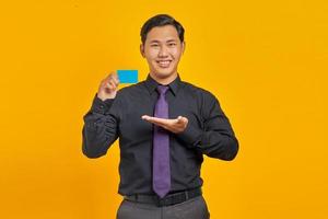 Alegre empresario asiático mostrando tarjeta de crédito sobre fondo amarillo foto
